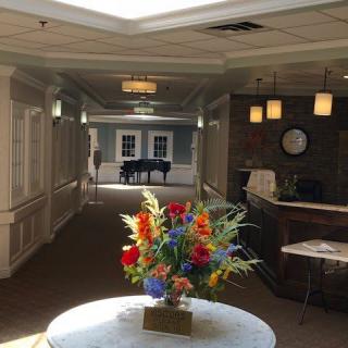 A brightly lit hallway with a bouquet of colorful flowers on a table and a piano in the background.