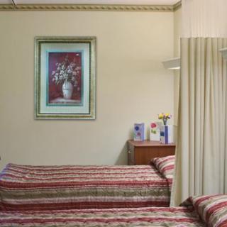 A cozy bedroom featuring two striped beds, a nightstand with decor, curtains, and a floral painting on the wall.