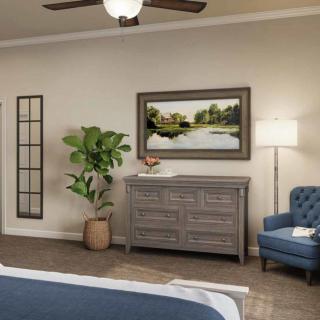 A cozy bedroom interior featuring a dresser, an armchair, a potted plant, and wall artwork under soft lighting.