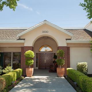 A front view of a building entrance with potted plants and neatly trimmed bushes.