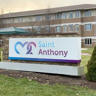 A sign for Saint Anthony hospital stands in front of a brick building.