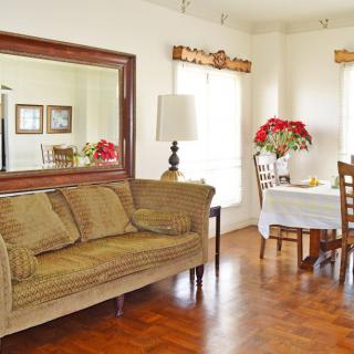A cozy living and dining area featuring a large mirror, comfortable sofa, dining table with chairs, and floral decorations.