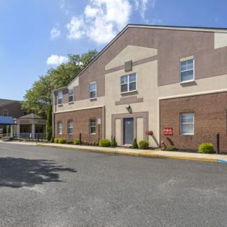 An exterior view of a building with an entrance and a parking lot under a partly cloudy sky.