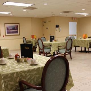 An empty dining room with tables set for service, featuring tablecloths and neatly arranged chairs.