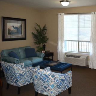 A cozy living room with a blue sofa, patterned chairs, and a large window with white curtains.