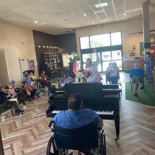 A musician in a wheelchair plays the piano for an audience in an indoor setting.