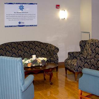 A cozy waiting room with patterned sofas and chairs arranged around a wooden coffee table, adorned with decorative pillows and soft lighting.