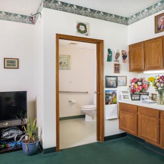 A living space with a view into the bathroom, featuring a television, cabinets, and decorative elements.