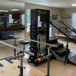 A rehabilitation gym featuring various exercise equipment, including parallel bars and weights.