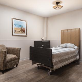 A minimalist bedroom with a single bed, armchair, and wall painting.