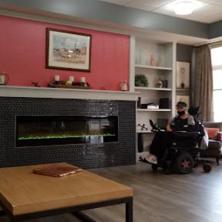 A cozy living room featuring a modern fireplace, comfortable furniture, and a person in a wheelchair enjoying the space.