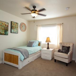 A cozy bedroom with a single bed, armchair, and bedside table under a ceiling fan.