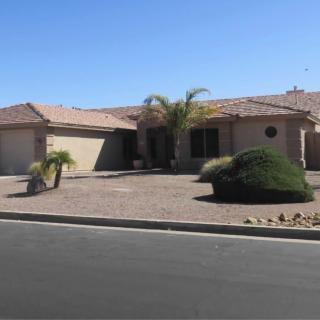 A single-story house in a suburban neighborhood with a desert landscape and palm trees.
