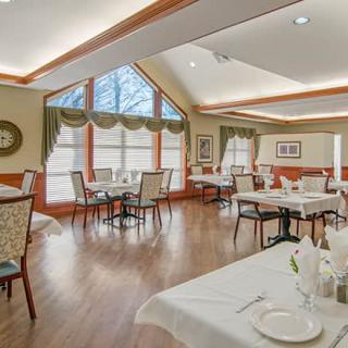 A cozy dining area with neatly arranged tables and chairs, illuminated by natural light from large windows.