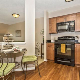 A cozy kitchen and dining area featuring modern appliances, a small round table with chairs, and wooden flooring.