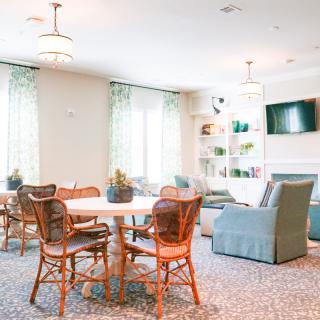 A cozy living room with a dining table, chairs, couch, and shelves, decorated in a light and airy style.