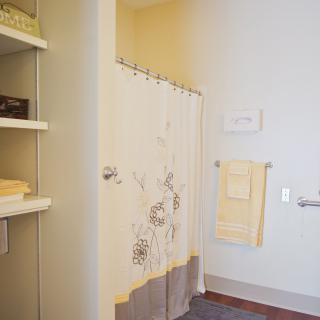 A neatly organized bathroom with a floral shower curtain, towels hung on the wall, and shelves with folded linens.