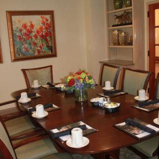 A dining room table elegantly set with cups and a floral centerpiece, surrounded by chairs and decorated with artwork.