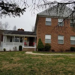 A charming two-story brick house featuring a welcoming front porch and a well-maintained yard.