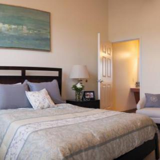 A cozy bedroom with a neatly made bed, bedside lamp, and wall artwork.