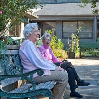 Two elderly women sitting on a bench, enjoying a sunny day outside.