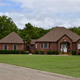 A suburban brick house with a well-maintained lawn and surrounding trees.