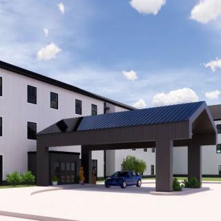 A modern hotel entrance with a driveway and car under a clear sky.