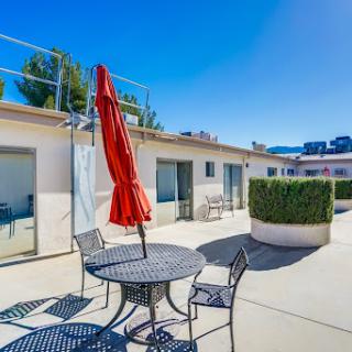 A sunny outdoor patio area with a table and chairs, featuring a vibrant red umbrella for shade.