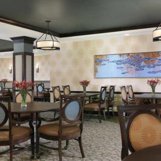 A well-decorated restaurant dining area with arranged tables and chairs, illuminated by elegant lighting fixtures and adorned with floral centerpieces and wall art.