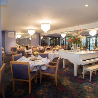 A cozy restaurant dining area featuring elegantly set tables and a white piano.