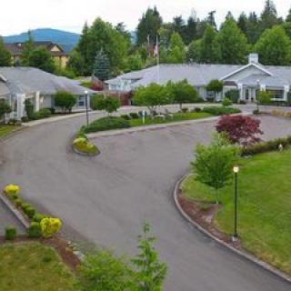 A scenic view of a residential facility surrounded by greenery and a curved driveway.