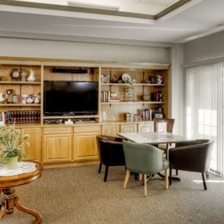 A cozy living room with a wooden bookshelf, television, and a small table surrounded by chairs.