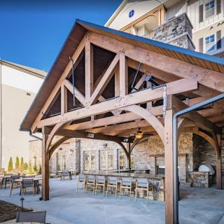 A charming outdoor patio area with a wooden canopy and seating arrangements, located adjacent to a building.