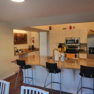 A modern kitchen with an open layout featuring a countertop with bar stools, appliances, and a cozy atmosphere.