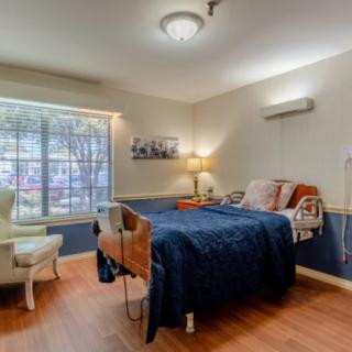 A cozy bedroom featuring a hospital bed, a comfortable chair, and a large window allowing natural light to fill the space.