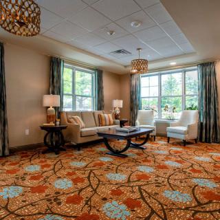 A cozy living room featuring a patterned carpet, comfortable seating, and large windows allowing natural light.