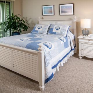 A cozy bedroom with a blue and white bedspread, nightstand, lamp, and framed artwork on the wall.