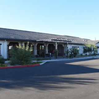 A single-story building with a tiled roof, surrounded by greenery and adjacent to a parking area.