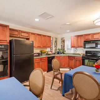 A cozy kitchen and dining area featuring wooden cabinets, black appliances, and tables adorned with blue tablecloths.