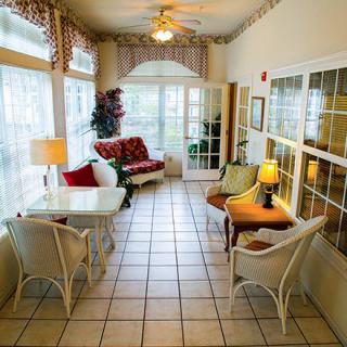 A cozy sunroom with ample natural light, featuring comfortable seating and tiled flooring.