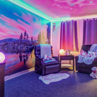 A vibrant and cozy living room with colorful mural walls, LED lighting, and comfortable armchairs.
