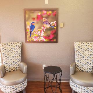 A cozy seating area featuring two stylish chairs and a vibrant piece of bird-themed artwork on the wall.