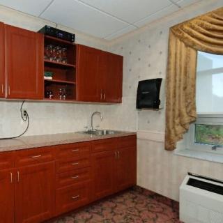 A small kitchen area with wooden cabinets and a sink, featuring a window with decorative curtains.