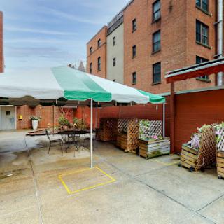 A cozy outdoor area featuring a green and white striped tent, surrounded by brick buildings and neatly arranged storage.