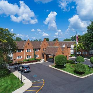 A brick building with a sloped roof and an adjacent parking lot under a partly cloudy sky.