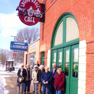 A group of people standing outside a caf with a distinctive sign, on a snowy day.