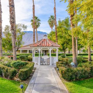 A charming gazebo surrounded by lush greenery and towering palm trees, set against a backdrop of mountains.