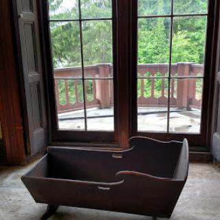 A vintage wooden cradle positioned near large windows, offering a serene view of the surrounding nature.