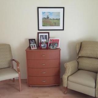A cozy corner with two chairs flanking a dresser topped with framed photos and a wall painting.