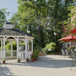 A peaceful outdoor patio area with a white gazebo and red umbrella surrounded by lush greenery.